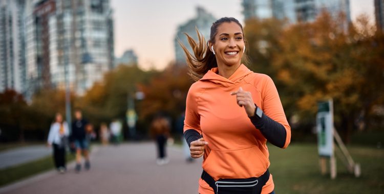 Young happy athletic woman listening music on earphones while jogging in the park.